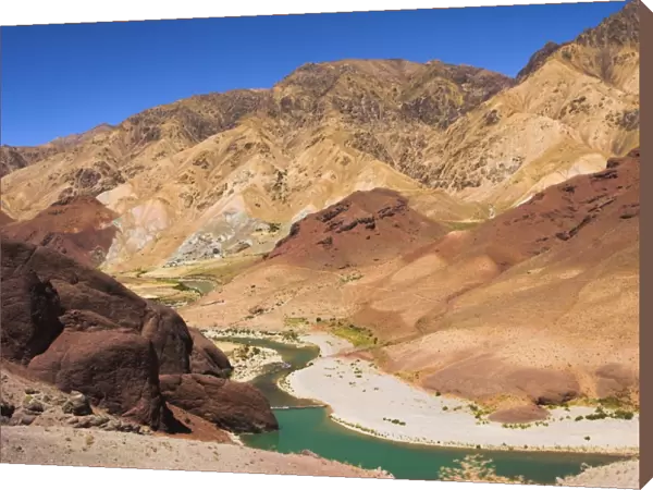 Hari Rud river flows through fertile valley at base of red rock mountains