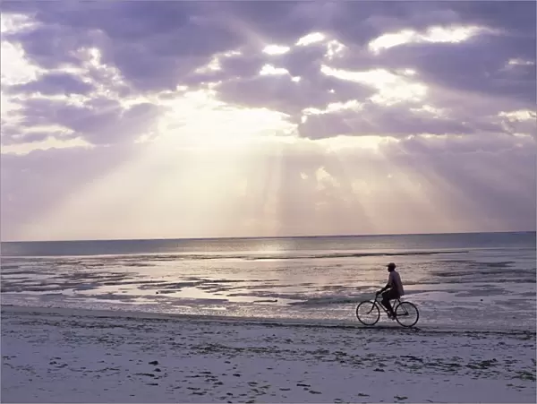 Fisherman cycling along the beach near Bweju against dramatic sky, island of Zanzibar