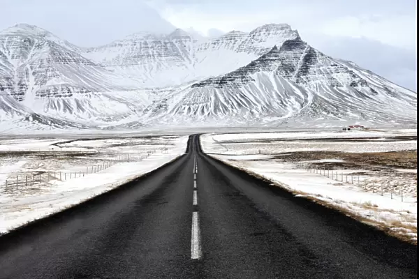 Black tarmac road leading towards snow covered mountains in winter, South Iceland
