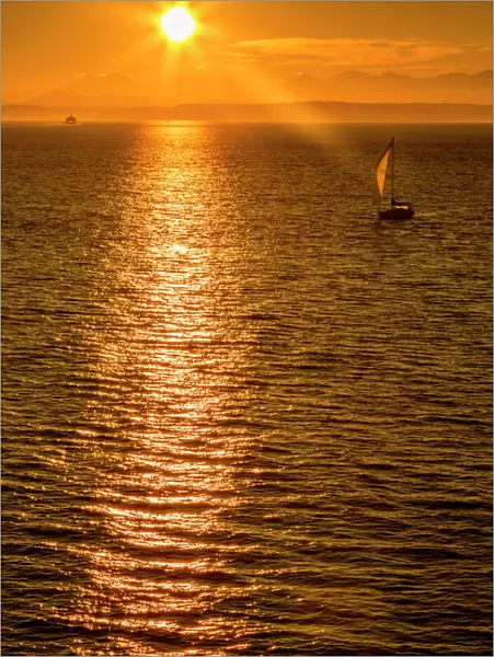 Sailing boat and sunset over Elliott Bay with Bainbridge Island visible on the horizon