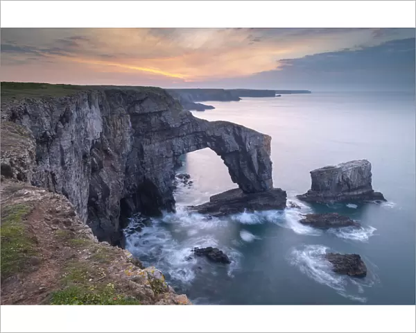 Colourful dawn sky above the Green Bridge of Wales natural arch in Pembrokeshire, Wales