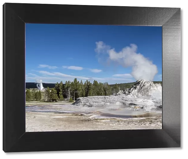 Castle Geyser steaming, with Old Faithful erupting behind, in Yellowstone National Park