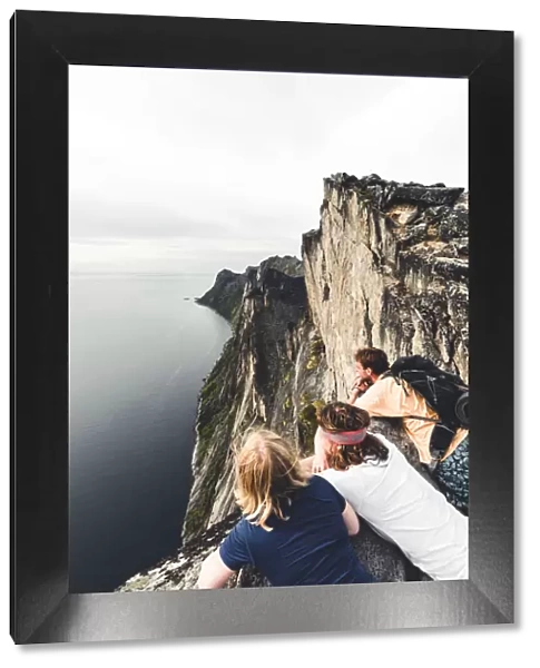 Three friends enjoying the view of the fjord leaning on rocks on Segla mountain peak