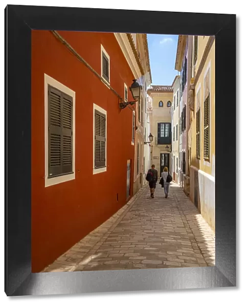 View of couple walking down pastel coloured street in historic centre, Ciutadella, Menorca, Balearic Islands, Spain, Mediterranean, Europe