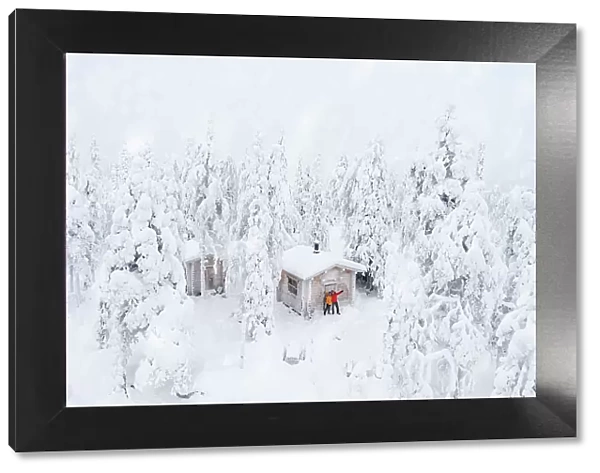 Aerial view of happy couple enjoying the winter holidays in a frozen hut in the snowy forest, Iso Syote, Northern Ostrobothnia, Lapland, Finland, Europe