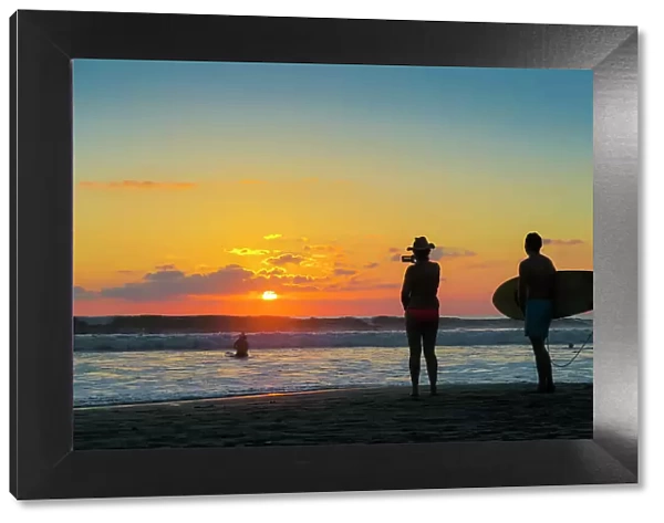 Surfer and woman photographing the sunset with smartphone on popular Guiones Beach, Playa Guiones, Nosara, Guanacaste, Costa Rica, Central America
