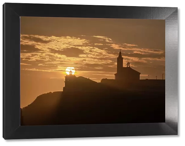 Sun aligned with the silhouette of the lighthouse and church of Luarca, Asturias, Spain, Europe