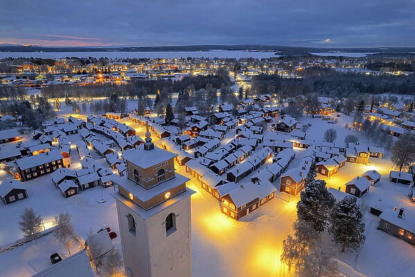 Aerial view of illuminated cottages and bell tower covered with snow in the old village of Gammelstad Church Town at dusk, UNESCO World Heritage Site, Lulea, Norrbotten, Norrland, Sweden, Scandinavia, Europe