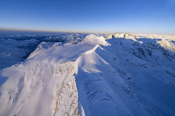 Aerial view of snowy peaks Piz Palu, Piz Zupo and Piz Bernina lit by sunrise, Engadine