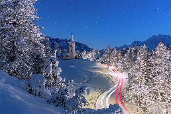 Car trails lights on snowy mountain road leading to Chiesa Bianca under the stars, Maloja, Engadine, Canton of Graubunden, Switzerland, Europe