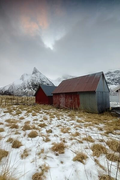 Clouds on snowy peaks above typical wooden hut called Rorbu, Senja, Ersfjord, Troms county
