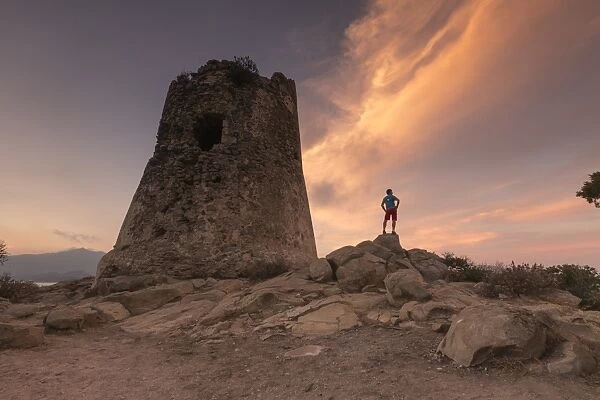 Hiker admires sunset from the stone tower overlooking the bay, Porto Giunco, Villasimius