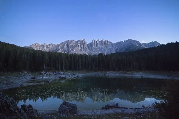 Latemar mountain range and woods are reflected in Lake Carezza at dusk, Ega Valley