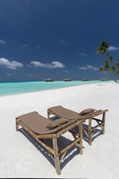 Lounge chairs and tropical beach, water villas and palm trees, Maldives, Indian Ocean