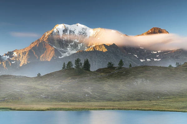 Majestic Fletschhorn and Galehorn peaks in autumn fog at dawn from Hopschusee lake