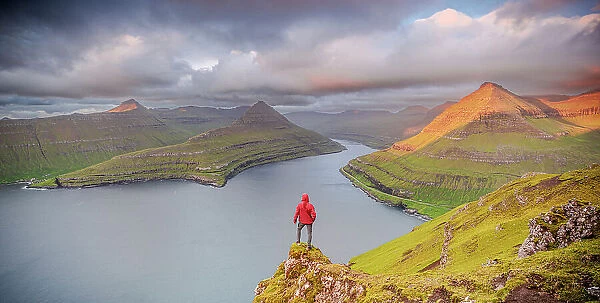 One man contemplating the sky at dawn standing on rocks above a fjord, Eysturoy Island, Faroe Islands, Denmark, Europe