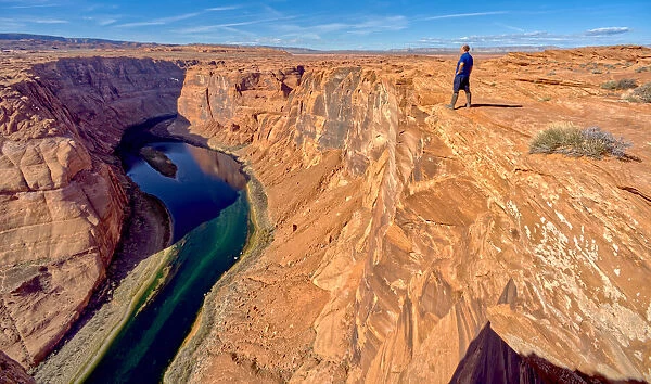 A man hiking on the edge of a cliff overlooking Horseshoe Bend near Page, Arizona