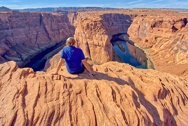 A man sitting on the edge of a cliff overlooking Horseshoe Bend near Page, Arizona