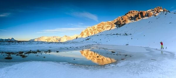 Panorama of Lake, Piz Umbrail at dawn with photographer in action framed by snow