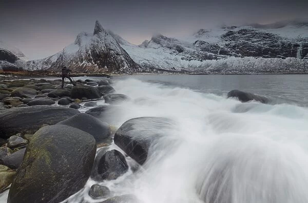 Photographer on the rocks surrounded by snowy peaks and waves of the cold sea, Senja