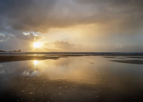 Rain clouds and reflections on Rhossili beach at sunset showing the shipwreck of the Helvetia, Rhossili, Gower, South Wales, United Kingdom, Europe