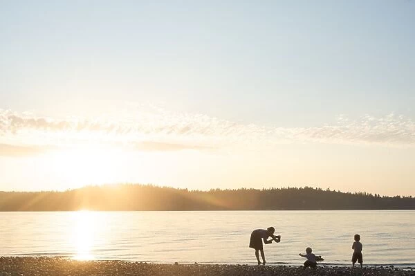 Silhouette of mother taking pictures of children at sunset, Vashon Island, Washington State, United States of America, North America