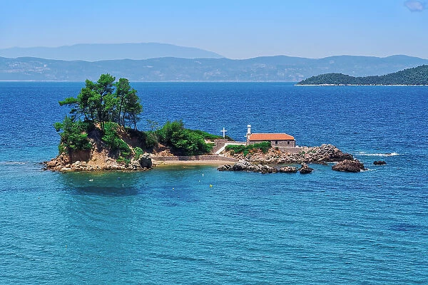 Small Christian church stone-built chapel with a cross on a small island strip in calm sea, Greek Islands, Greece, Europe