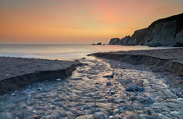 A stream cuts across sand as it reaches the sea, at dusk, in Ayrmer Cove, a remote cove near Kingsbridge, south coast of Devon, England, United Kingdom, Europe