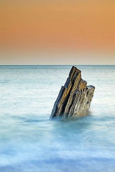 A sunset view of a jagged tooth-like rock, surrounded by surging sea at Ayrmer Cove, a remote cove near Kingsbridge, south coast of Devon, England, United Kingdom, Europe