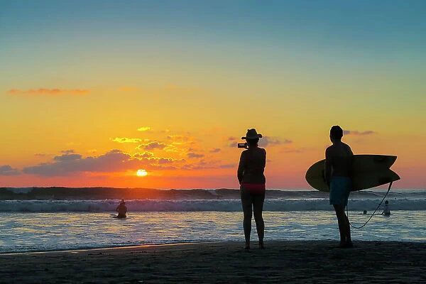 Surfer and woman photographing the sunset with smartphone on popular Guiones Beach, Playa Guiones, Nosara, Guanacaste, Costa Rica, Central America