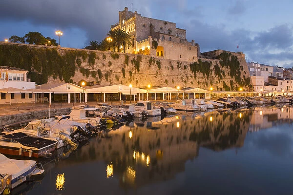 View across tranquil harbour to the illuminated Town Hall at dusk, Ciutadella (Ciudadela)