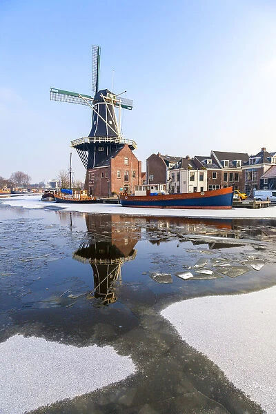 Windmill De Adriaan reflected in the canal of icy river Spaarne, Haarlem