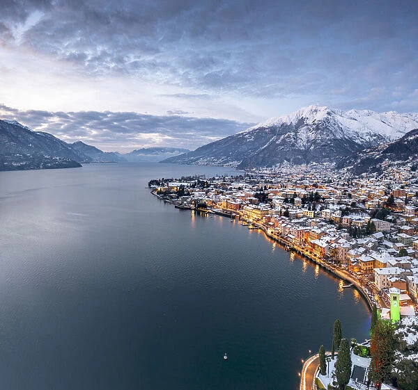 Winter sunrise over the illuminated lakeside town of Gravedona and snowy peaks, Lake Como