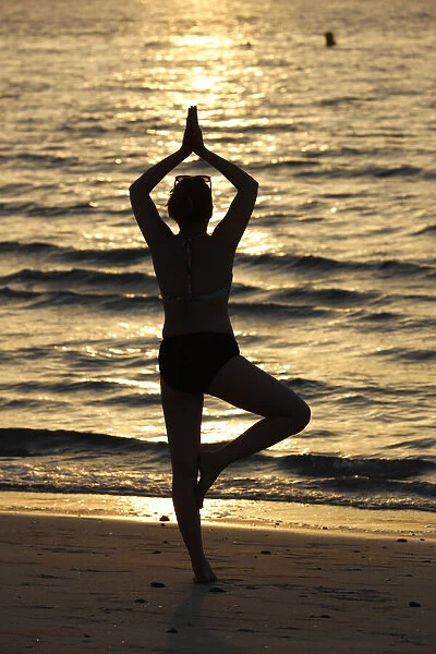 Woman practising yoga meditation on beach at sunset as concept for silence and relaxation