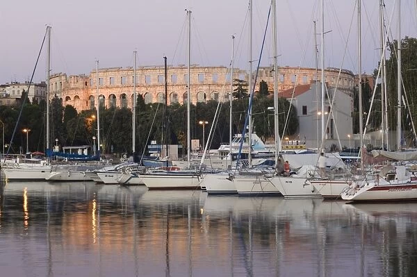 Yachts in the harbour, with the 1st century Roman amphitheatre beyond in evening light