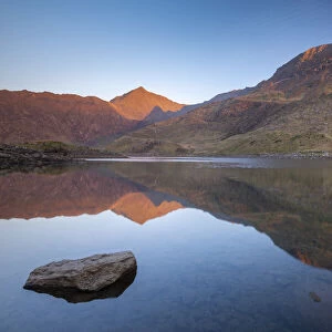 Mount Snowdon bathed in the first light of dawn in spring and reflected in Llyn Llydaw