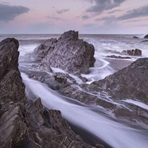 Waves surge around the jagged rocks on Wildersmouth Beach, Ilfracombe, Devon, England