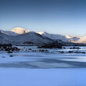 Winter view at dawn over frozen Lochain Na h Achlaise to sun-kissed Black Mount hills