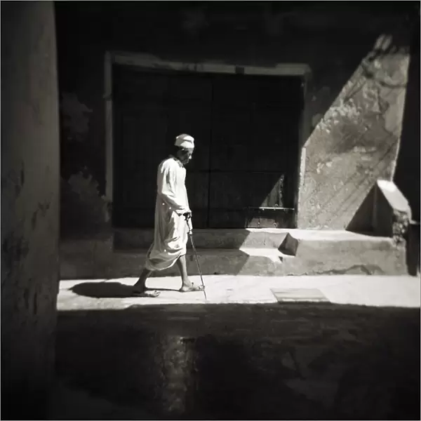 Image taken with a Holga medium format 120 film toy camera of a man in white djellaba caught in sunlight in backstreets of Stonetown, Zanzibar, Tanzania, East