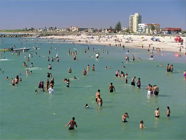 Groups of people in the sea and on the beach at Glenelg, a resort suburb of Adelaide