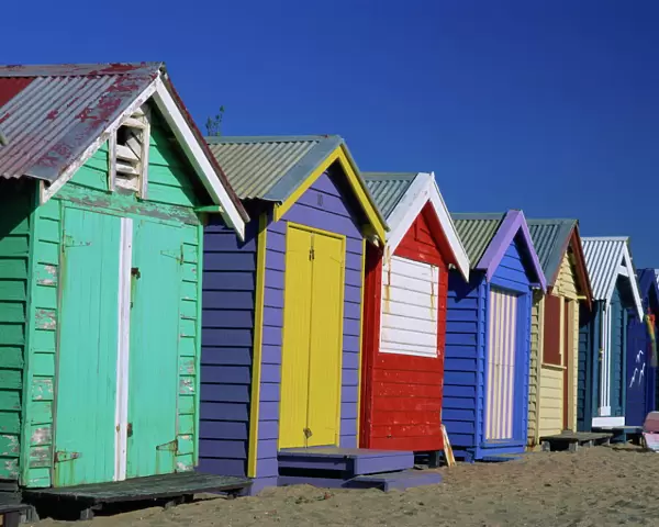 Exterior of a row of beach huts painted in bright primary colours, Brighton Beach