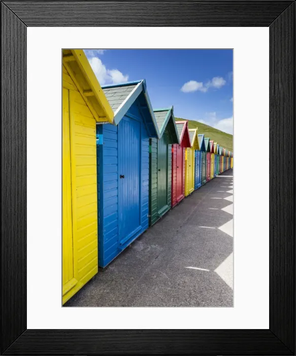 Framed Print : Row of colourful beach huts and their shadows with green hill backdrop, West Cliff Beach Framed Print : Row of colourful beach huts and their shadows with green hill backdrop, West Cliff Beach