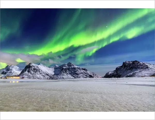 Northern Lights (aurora borealis) illuminate the sky and the snowy peaks, Flakstad