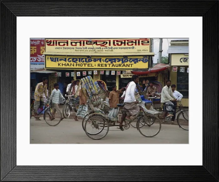 Framed Print : Men riding cycle rickshaws on the street passing the outside of a hotel Framed Print : Men riding cycle rickshaws on the street passing the outside of a hotel