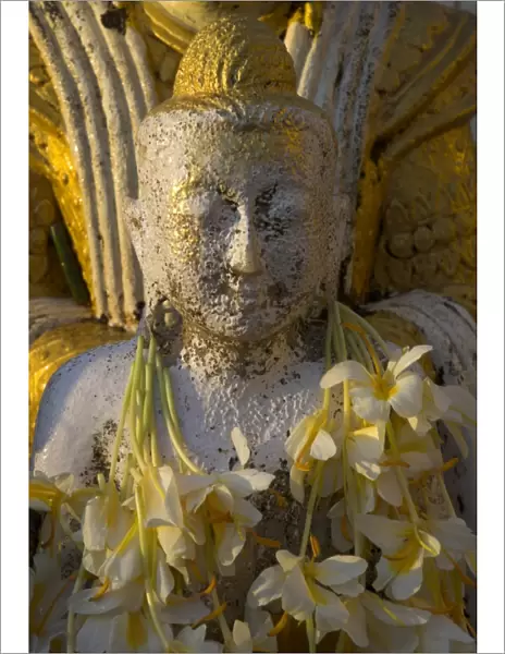 Close up of small Buddha figure with flowers round the neck in the Shwedagon Paya