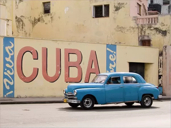 A vintage 1950s American car passing a Viva Cuba sign painted on a wall in cental Havana, Cuba, West Indies