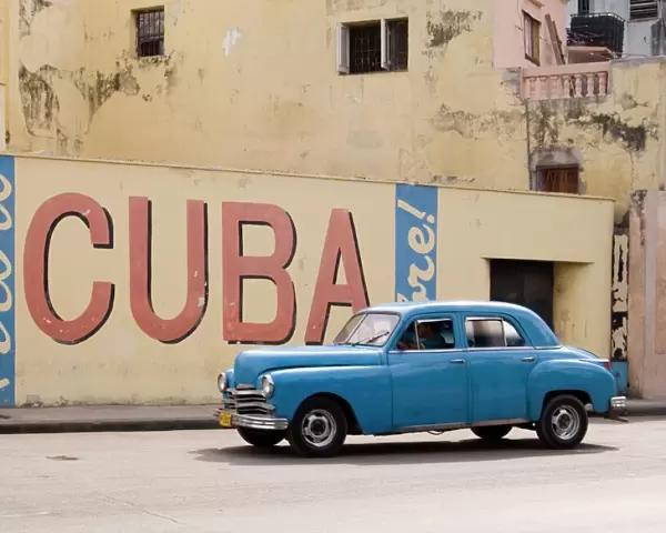 A vintage 1950s American car passing a Viva Cuba sign painted on a wall in cental Havana, Cuba, West Indies