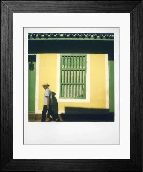 Framed Print : Polaroid of man walking past yellow wall with painted green window grille
