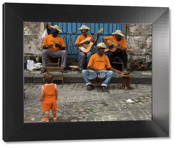Street band wearing orange shirts playing music on the pavement watched by toddler wearing orange clothes, Habana Vieja (Old Havana), Havana, Cuba, West Indies