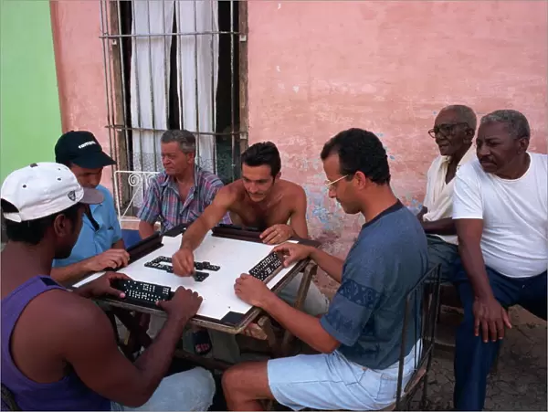A group of men sitting around a table playing dominoes outdoors, Trinidad